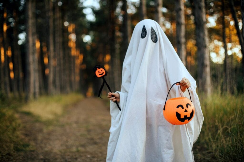 How to make a ghost costume for Halloween: Girl wearing ghost costume holding pumpkin bucket with candies