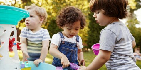 Group Of Young Children Playing With Water Table In Garden