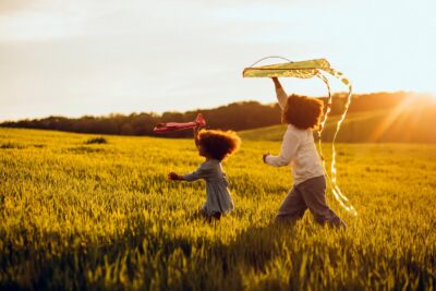Two kids flying a kite in a field at sunset