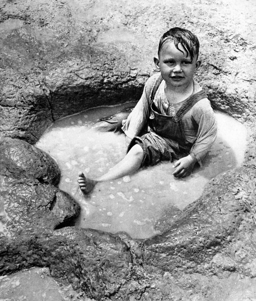 Vintage photo of boy sitting in a huge ancient dinosaur footprint 